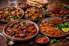 Assorted Indian dishes including curries and roasted meats on a wooden table.