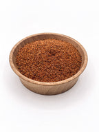 Wooden bowl filled with brown spice mix on a white background